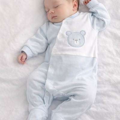 Bebé a dormir com macacão azul claro bordado com ursinho em fundo branco