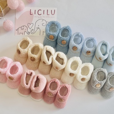 Sapatinhos de tricô para bebé de várias cores com botões de madeira ao lado de cartão LICILU