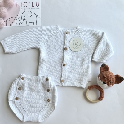 Conjunto de bebé branco em malha com casaco e tapa-fraldas, brinquedo de raposa em crochet e papel com elefantes e texto LICILU.