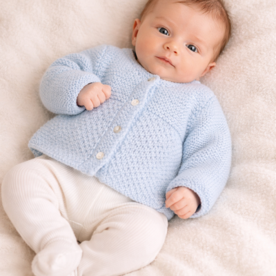 Bebé deitado com camisola azul clara e calças brancas numa manta creme macia