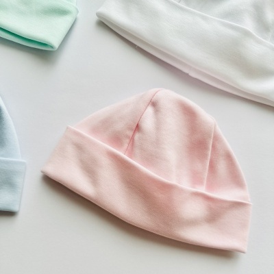Gorros de algodão para bebé em cores pastel sobre superfície branca