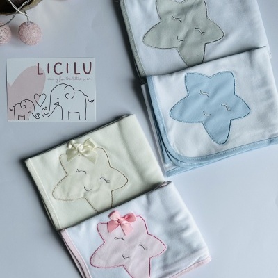 Mantinhas para bebé com estrelas sorridentes em cinza, azul, bege e rosa, com laços, sobre superfície branca e cartão LICILU.