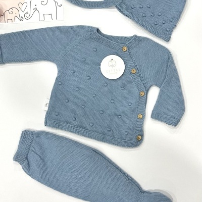 Conjunto de bébé azul em malha com camisola, calças e touca ao lado de embalagem com texto LICILU