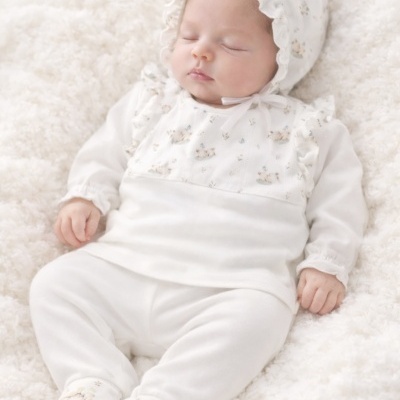 Bebé vestido com conjunto branco de padrão com pequenos ursos e flores em tons pastel adormecido numa manta branca texturada.