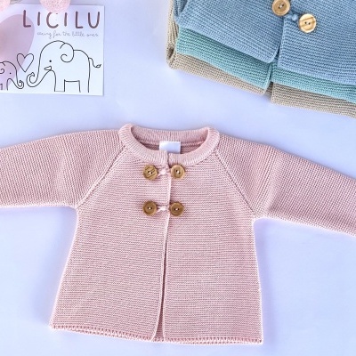 Casaco infantil de malha rosa com botões de madeira sobre superfície branca