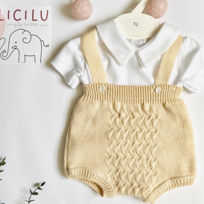 Conjunto de bebé com body branco e jardineira de malha bege com padrão trançado.