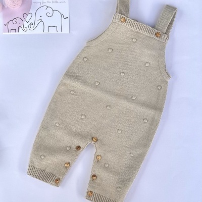 Macacão de bebé bege em malha com botões de madeira e textura de pompons, cartão LICILU ao lado.