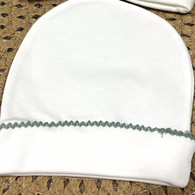 Touca branca de tecido com costura decorativa verde sobre superfície bege com padrão