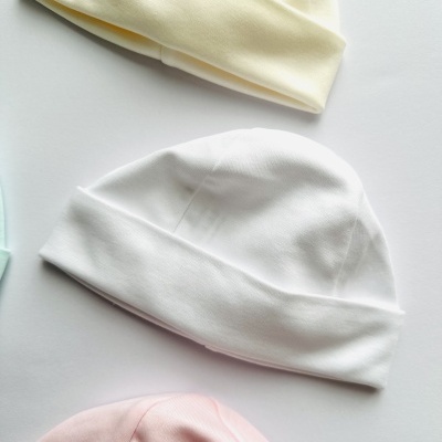 Gorros para bebé em algodão de cores claras sobre fundo branco.