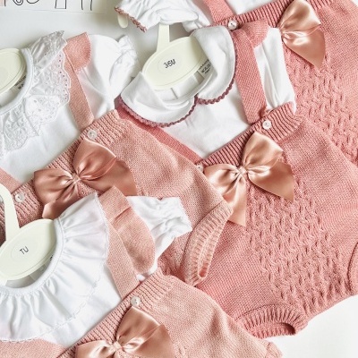 Três conjuntos de roupa de bebé com bodies brancos e calções/petitos rosa com laços.