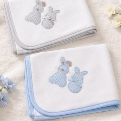 Duas mantas de bebé brancas com bordados de coelhinhos em cinza e azul sobre tecido macio creme.