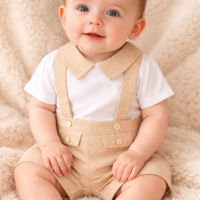 Bebé vestido com fato bege e t-shirt branca sentado numa manta macia bege