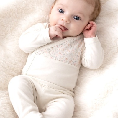 Bebé com fato de corpo creme e padrão floral deitado em tecido branco macio