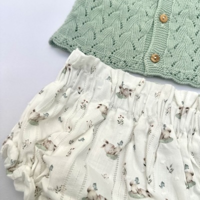 Conjunto infantil de camisola verde de malha e cueiro branco com padrão de coelhos.