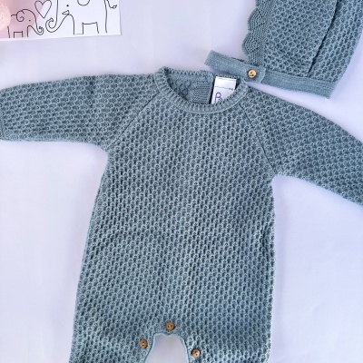 Fato de bebé em tricô azul cinzento com padrão texturizado e gorro, sobre fundo branco com cartão decorativo