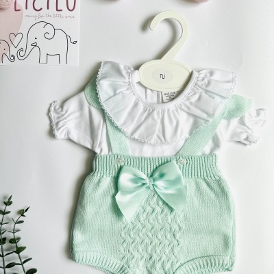 Conjunto de roupa para bebé branco e verde água pendurado num cabide branco