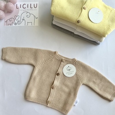 Camisolas de malha para bebé em várias cores com botões frontais e etiquetas, sobre superfície branca