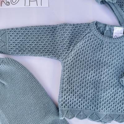 Conjunto de roupa de bebé azul em malha com touca e calças sobre fundo branco com ilustração de elefantes