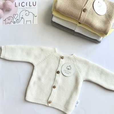 Casaco de malha infantil creme com botões de madeira e outros casacos coloridos ao lado.