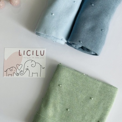 Três mantas tricotadas azul claro, azul médio e verde com pequenas bolinhas, cartão LICILU e guirlanda de bolas cor de rosa
