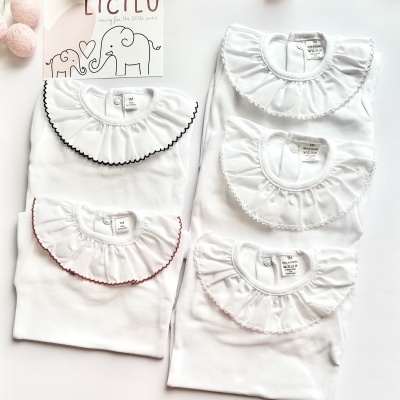 Bodies brancos para bebé com golas frisadas e bordados, marca LICIU, dispostos em fundo branco com decoração de luzes. 
