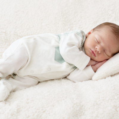 Bebé recém-nascido dormindo vestido com body branco com padrão xadrez verde deitado sobre almofada branca macia