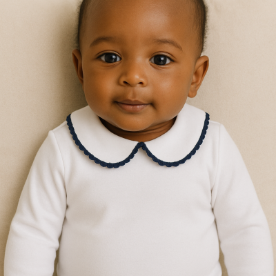 Bebé com body branco de gola bordada azul sentada em sofá bege