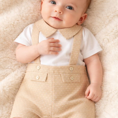 Bebé vestido com fato bege de suspensórios e t-shirt branca, deitado em manta felpuda creme.