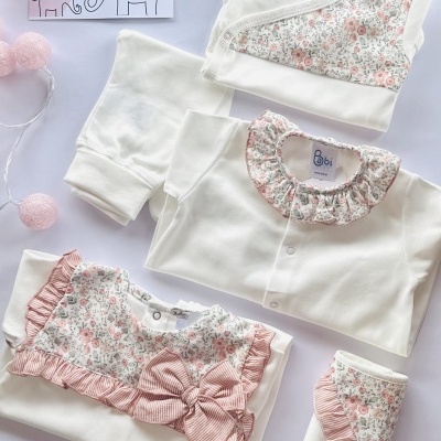 Conjunto de roupa de bebé branca com detalhes florais e laço e manta com padrão floral