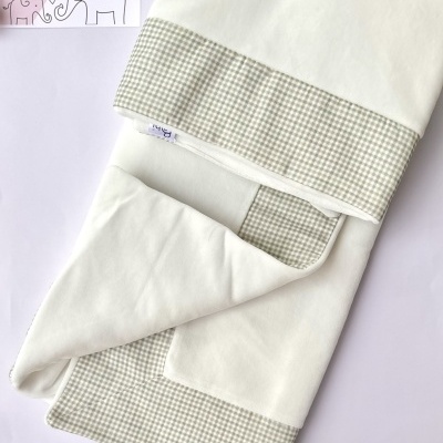 Manta branca para bebé com detalhes em xadrez bege e branco, cartão LICILU ao lado