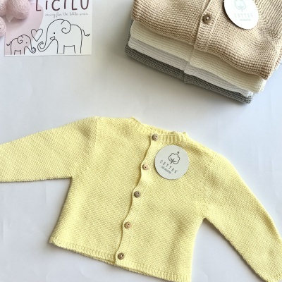 Casaco de bebé amarelo claro em malha com botões de madeira e outras peças dobradas ao lado