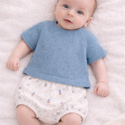 Bebé deitado com camisola azul de malha e calções estampados de barcos