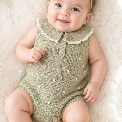 Bebé sorridente com roupa de malha verde clara e fita de cabelo creme