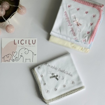 Fraldas bordadas com texto e cartão LICILU sobre mesa branca.