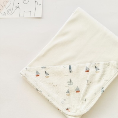 Fralda branca com padrão de barcos coloridos e farol, etiqueta LICILU com elefante.