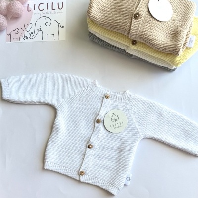 Casaco de malha branco para bebé com botões, junto a casacos empilhados coloridos e cartão LICILU
