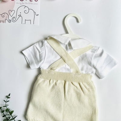 Roupa de bebé branca e creme com suspensórios em cabide