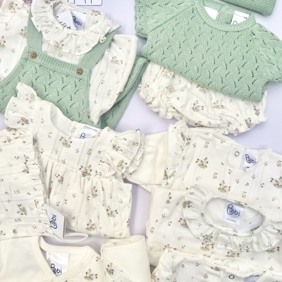 Roupas de bebé em algodão creme com estampado de coelhinhos e malha verde com textura, sobre fundo branco com cartão de marca.