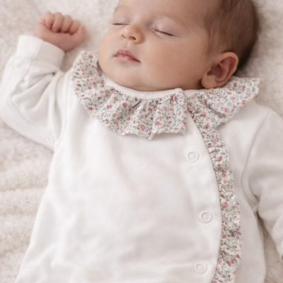 Bebé a dormir com babygrow branco com babados florais.
