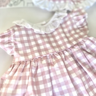 Vestido infantil xadrez rosa e branco com gola de renda em fundo branco com placa decorativa