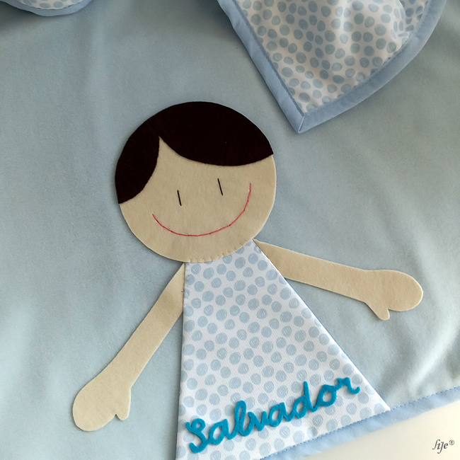 Colcha azul claro com boneco aplicado e nome Salvador costurado.
