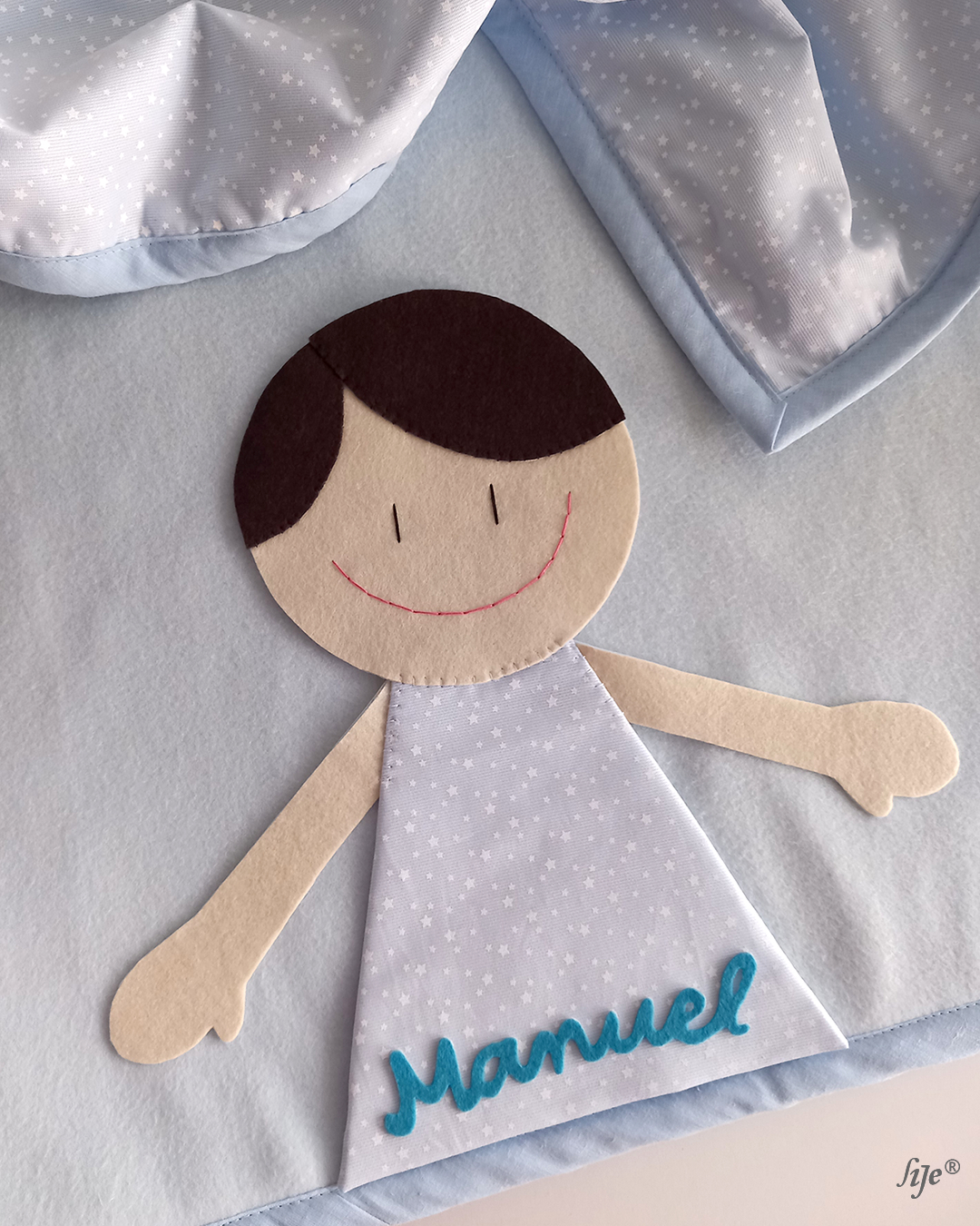 Tecido para bebé com figura de menino em feltro e vestido azul com estrelas e nome Manuel.