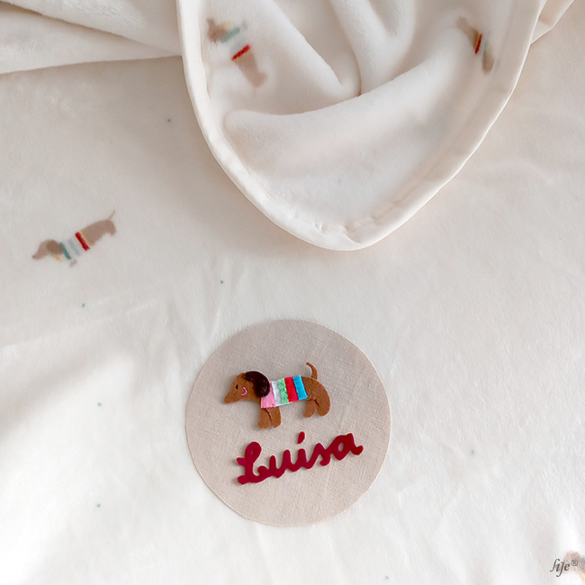 Manta branca com cães castanhos e etiqueta com cão em feltro e nome Luisa