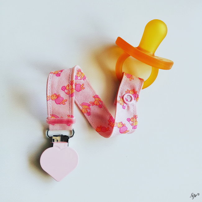 Chupeta amarela com fita rosa decorada com doces e presa metálica em forma de coração