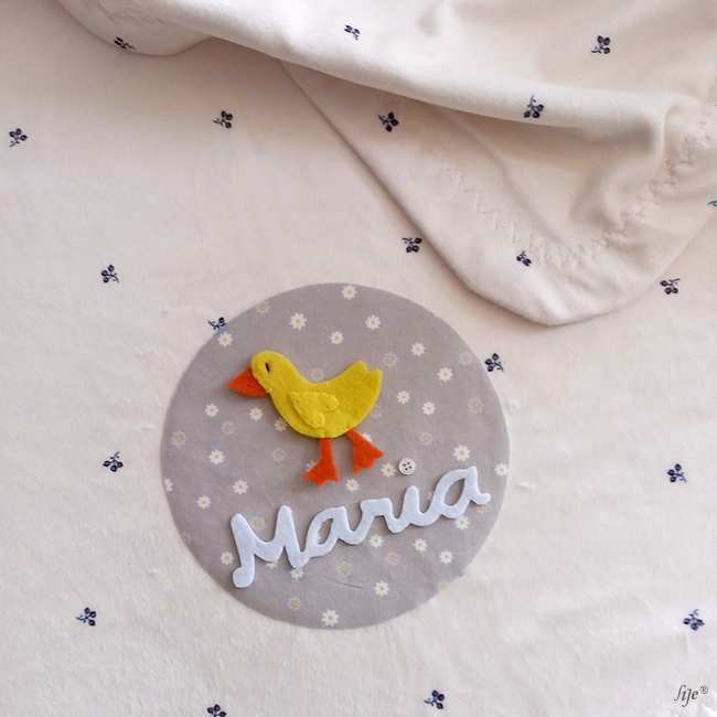 tecido bege claro com pato amarelo de feltro e nome Maria bordado