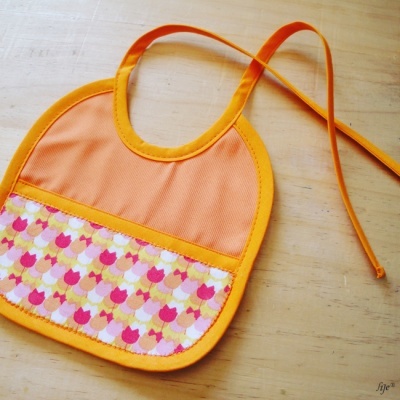 Babete para bebé laranja com padrão colorido sobre madeira clara