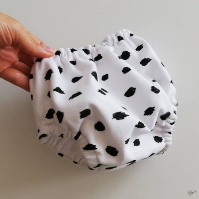 Cueca ou fralda de tecido branco com manchas pretas, texturizada e segurada por uma mão