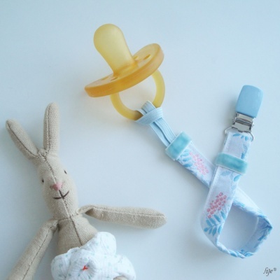 Chupeta amarela com fita azul com padrão floral e clip azul junto a boneco de coelho de tecido macio