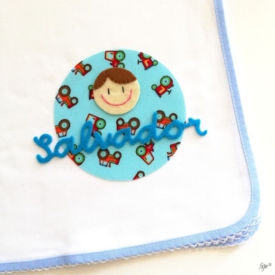 Fralda branca com borda azul e apliques de tecido, incluindo carinha sorridente e nome 'salvador' em feltro azul