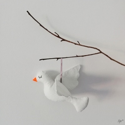 Enfeite de pássaro branco de tecido pendurado num ramo seco